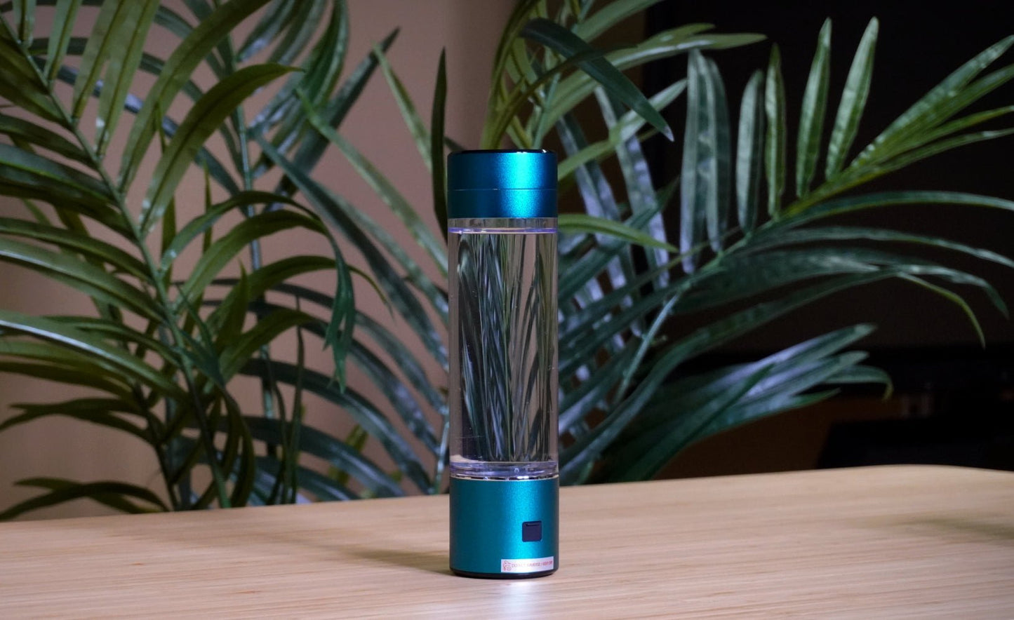HydroSmart - H2 Essence H2 Essence BLU - 1HydroSmart, H2 Essence hydrogen vandflaske på træbord med grønne planter i baggrunden, fremhæver naturlig og økologisk appel.