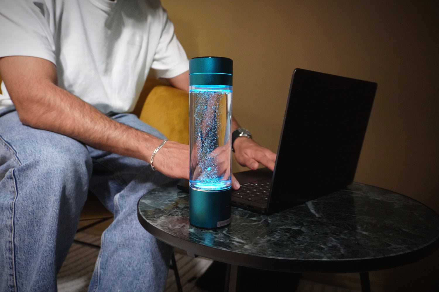 Mand bruger en bærbar computer med en HydroSmart hydrogen vandflaske på bordet, der viser flaskens elegante design og teknologi i en hjemmeindstilling.
