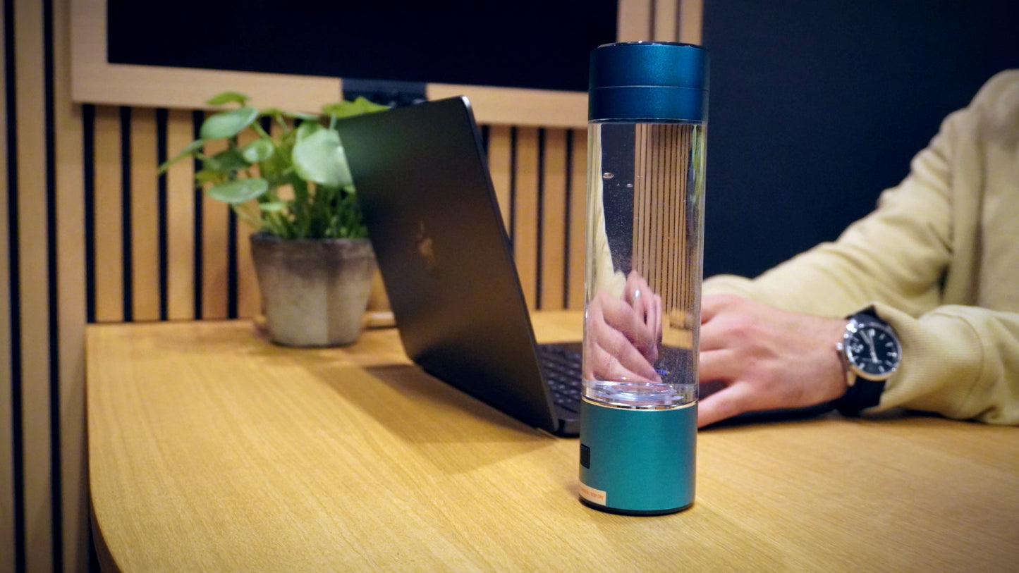 HydroSmart - H2 Essence H2 Essence BLU - 1H2Essence hydrogenflaske placeret på et arbejdsbord ved siden af en bærbar computer. Ideel til brug på kontoret, der kombinerer funktionelt design og sundhedsmæssige fordele med hydrogenberiget vand.